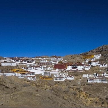 The ancient Ganden Monastery perched on a hillside, with prayer flags fluttering in the wind.