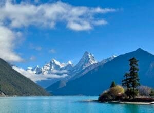 Basum Lake during Tibet Peach Blossom Festival, with turquoise water under the blue sky and snow-capped mountains in the background.