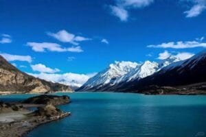 Serene Ranwu Lake with turquoise waters and snowy mountains in the distance during Tibet’s Peach Blossom Festival.
