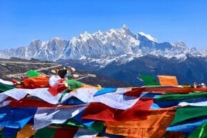 Prayer flags fluttering in the wind at Sejila Mountain Pass in Tibet, with snow-capped peaks under the blue sky.