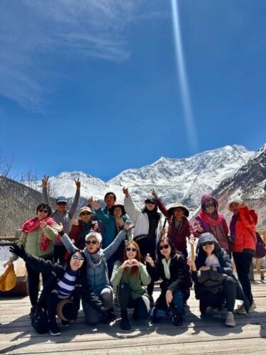 Happy travelers posing at the Karola Glacier under the bright blue sky, with the glacier as a stunning backdrop.