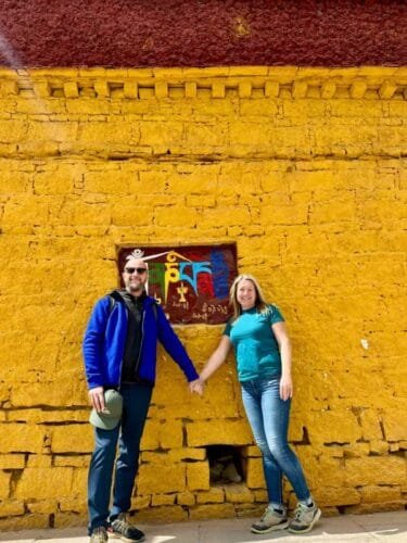 Travelers standing by a temple wall inscribed with Tibetan mantras