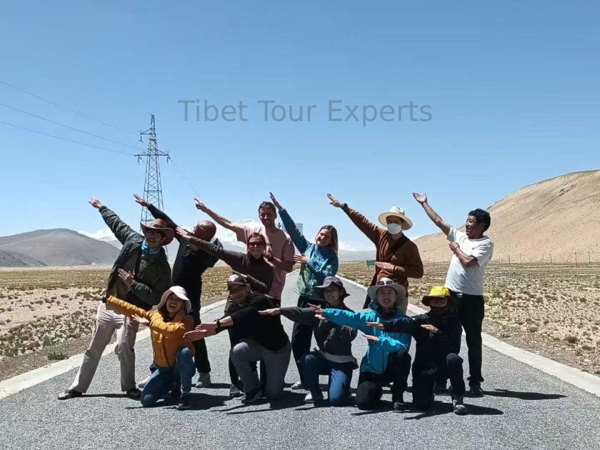 Happy travelers with their guide on the way to Mount Everest and Mount Kailash, raising their right hands towards the sky in a joyful pose.