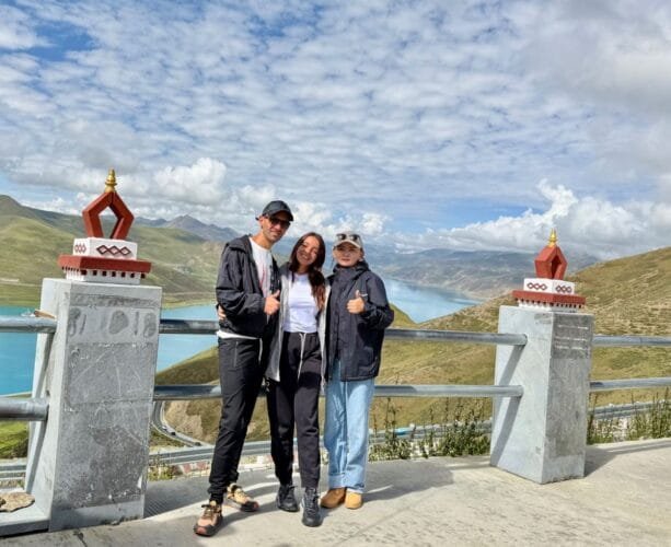 Travelers enjoying the panoramic view of Yamdrok Lake from the viewing platform, smiling and giving thumbs up.
