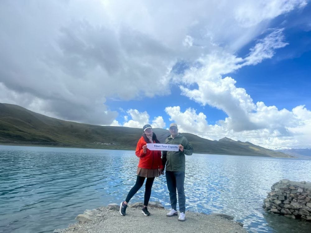 Travelers holding a Tibet Tour Experts banner by the turquoise Yamdrok Lake in Tibet.